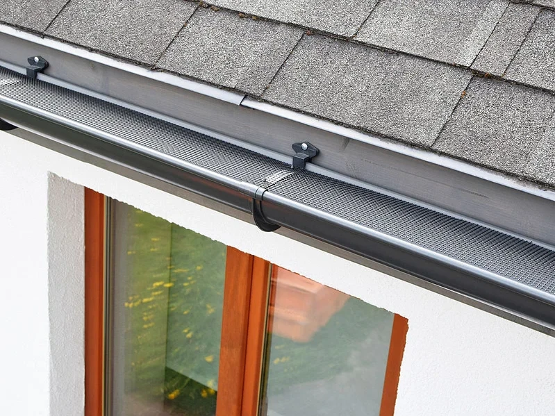 Close-up of a dark gray seamless gutter with a mesh leaf guard installed on a house