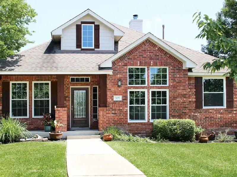 Vinyl Window Replacement — Front exterior of a brick house with multiple white-framed windows and dark shutters
