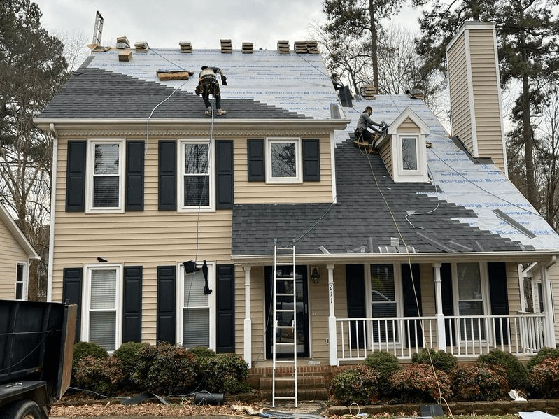 Roofers installing new dark gray shingles and underlayment on a two-story house
