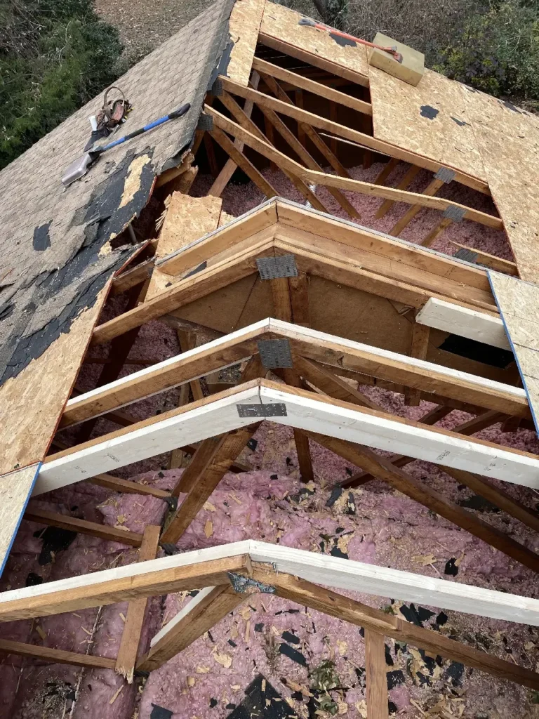 Damaged roof with exposed wooden trusses and pink insulation, indicating significant damage