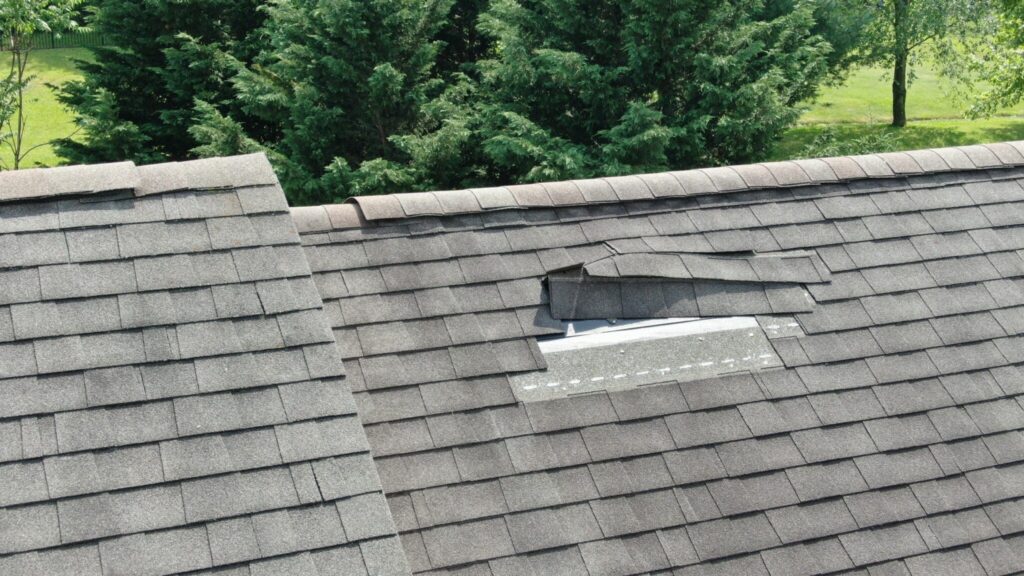 Storm Damage Repair — Close-up of a gray shingle roof with a section of shingles lifted and missing, exposing the underlaymen