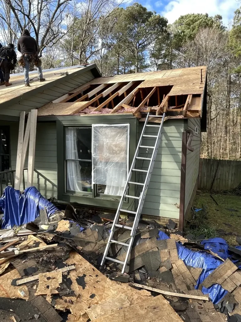 House with a partially removed roof and exposed rafters, surrounded by roof debris