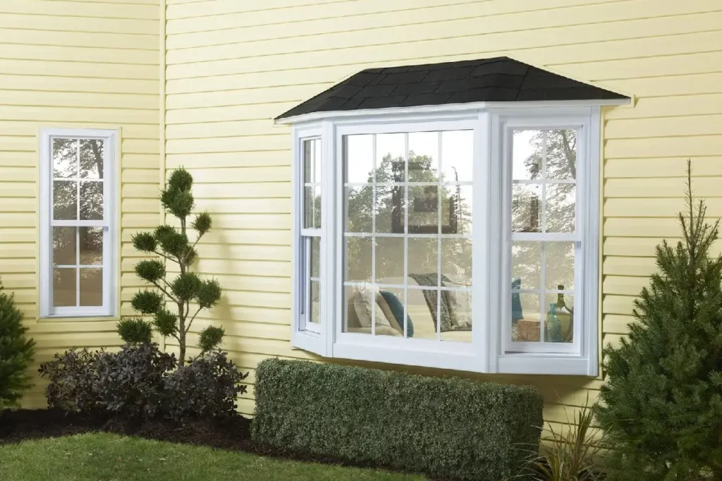 Exterior view of a white-framed bay window and a single vertical window on a yellow siding house